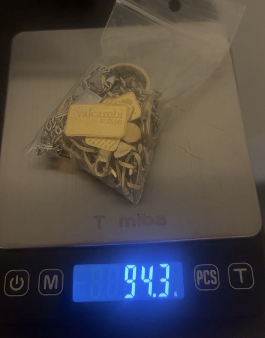 Gold jewellery and a small bar in a clear bag above a blue scale display
