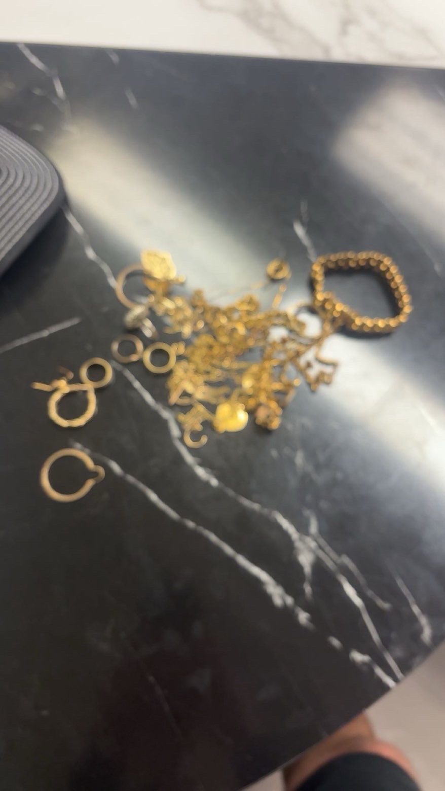 Small gold rings, chains and pendants on a reflective dark table