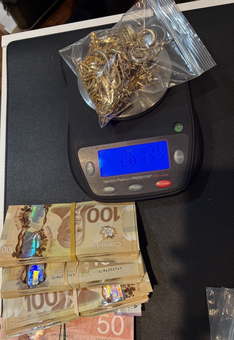 Bagged gold on a blue-display scale beside stacks of Canadian banknotes