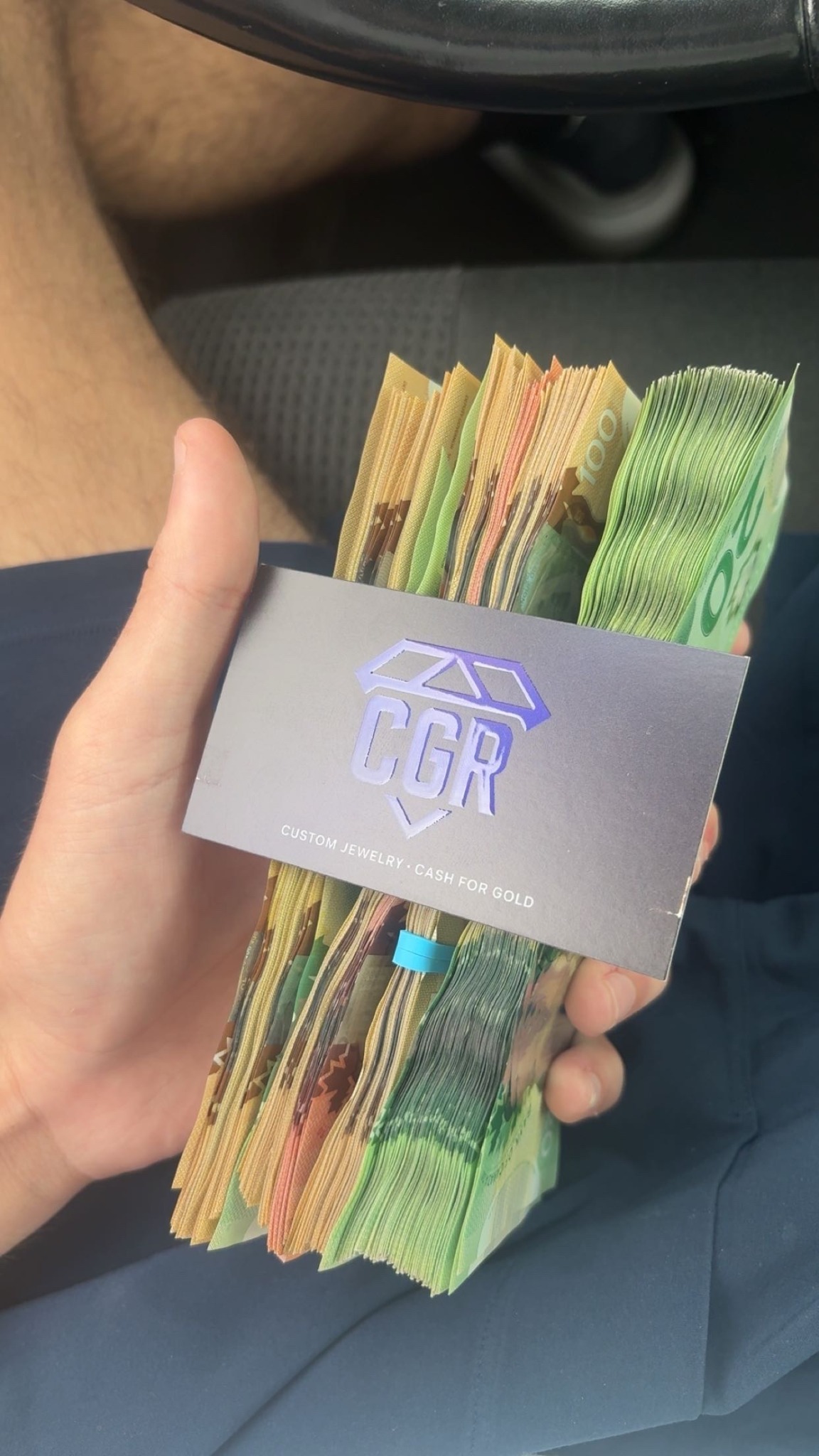 A hand holding Canadian banknotes and a purple CGR Jewellers business card