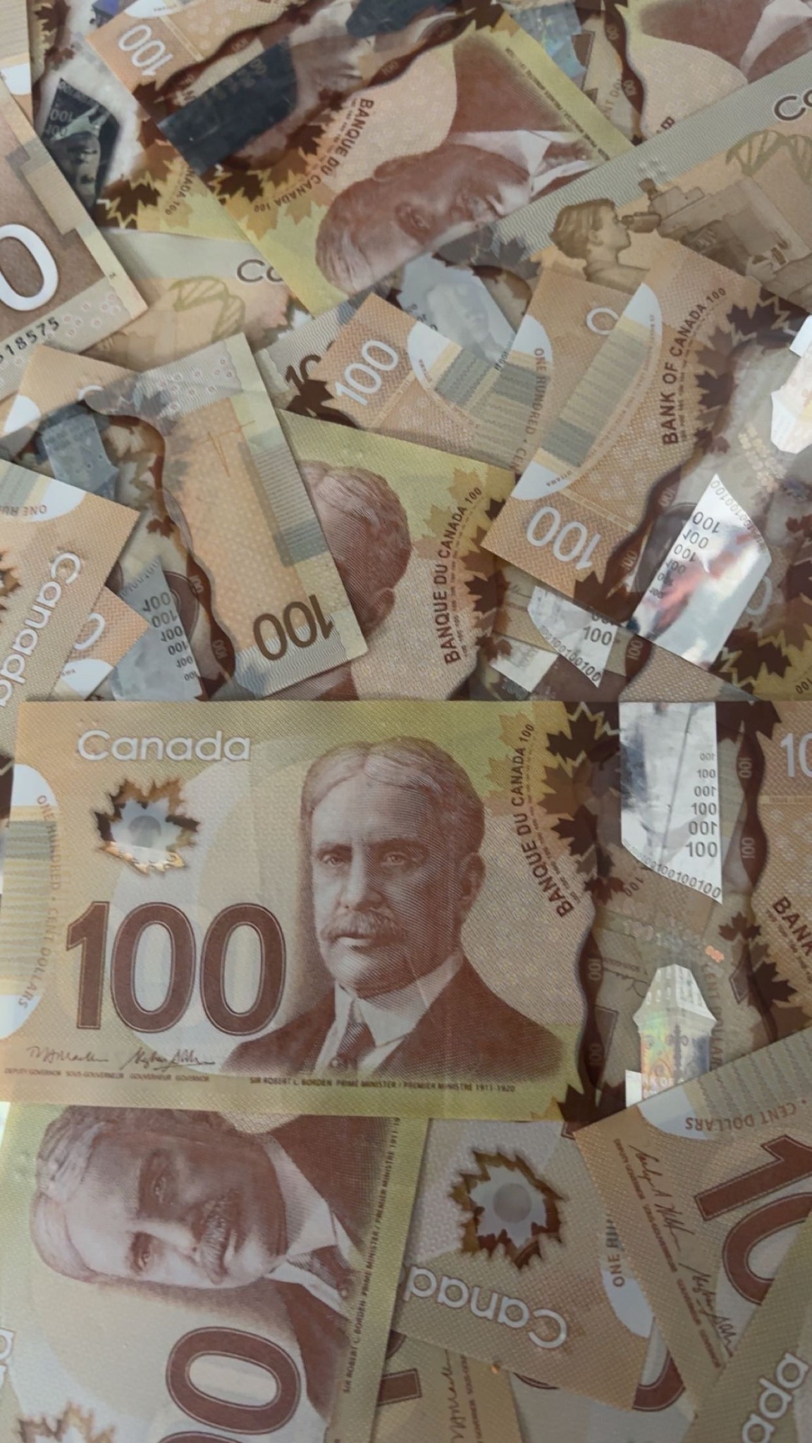 Canadian one-hundred-dollar banknotes spread across a dark surface