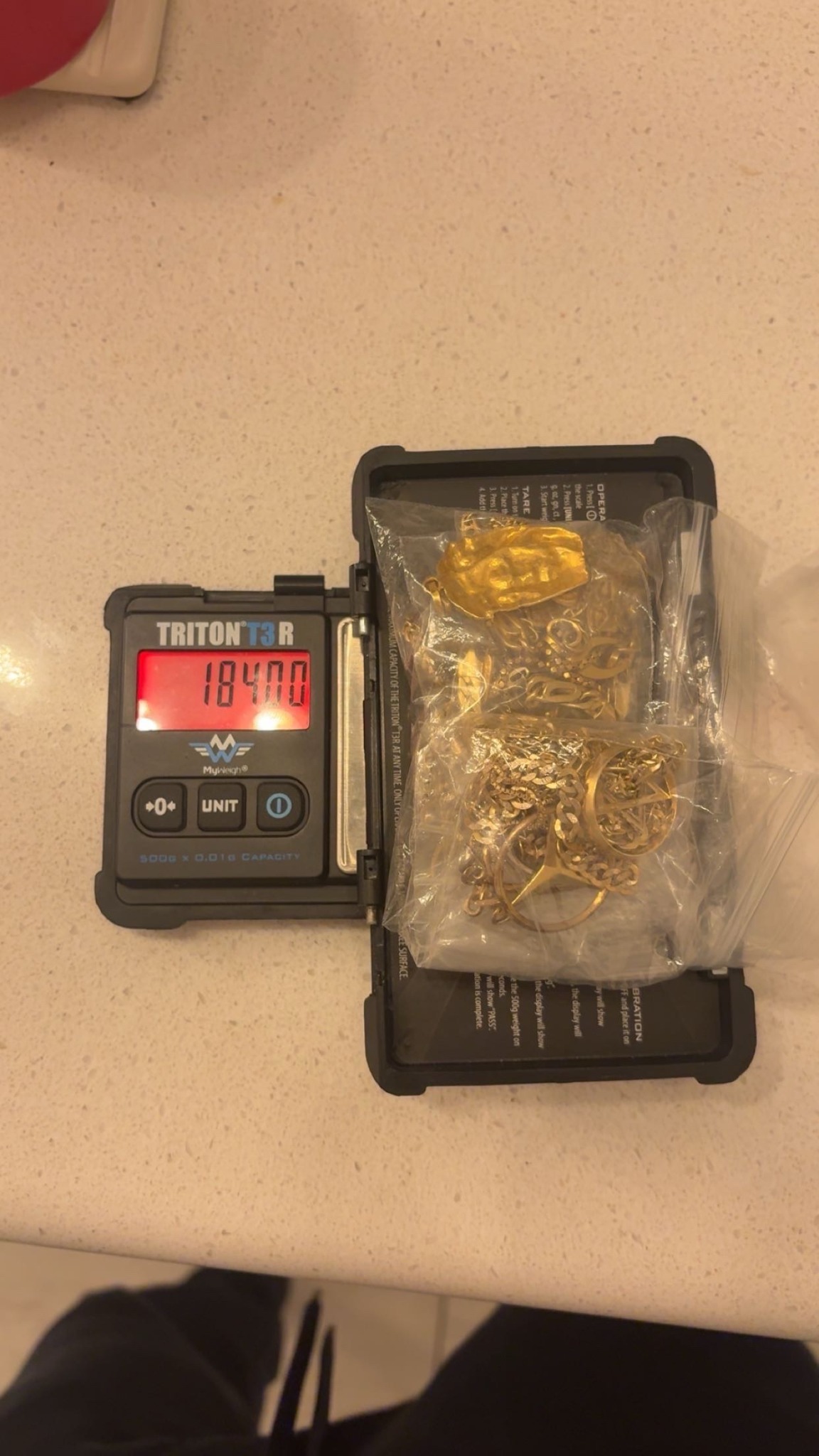 A clear bag of gold jewellery on a red digital scale showing 184.00